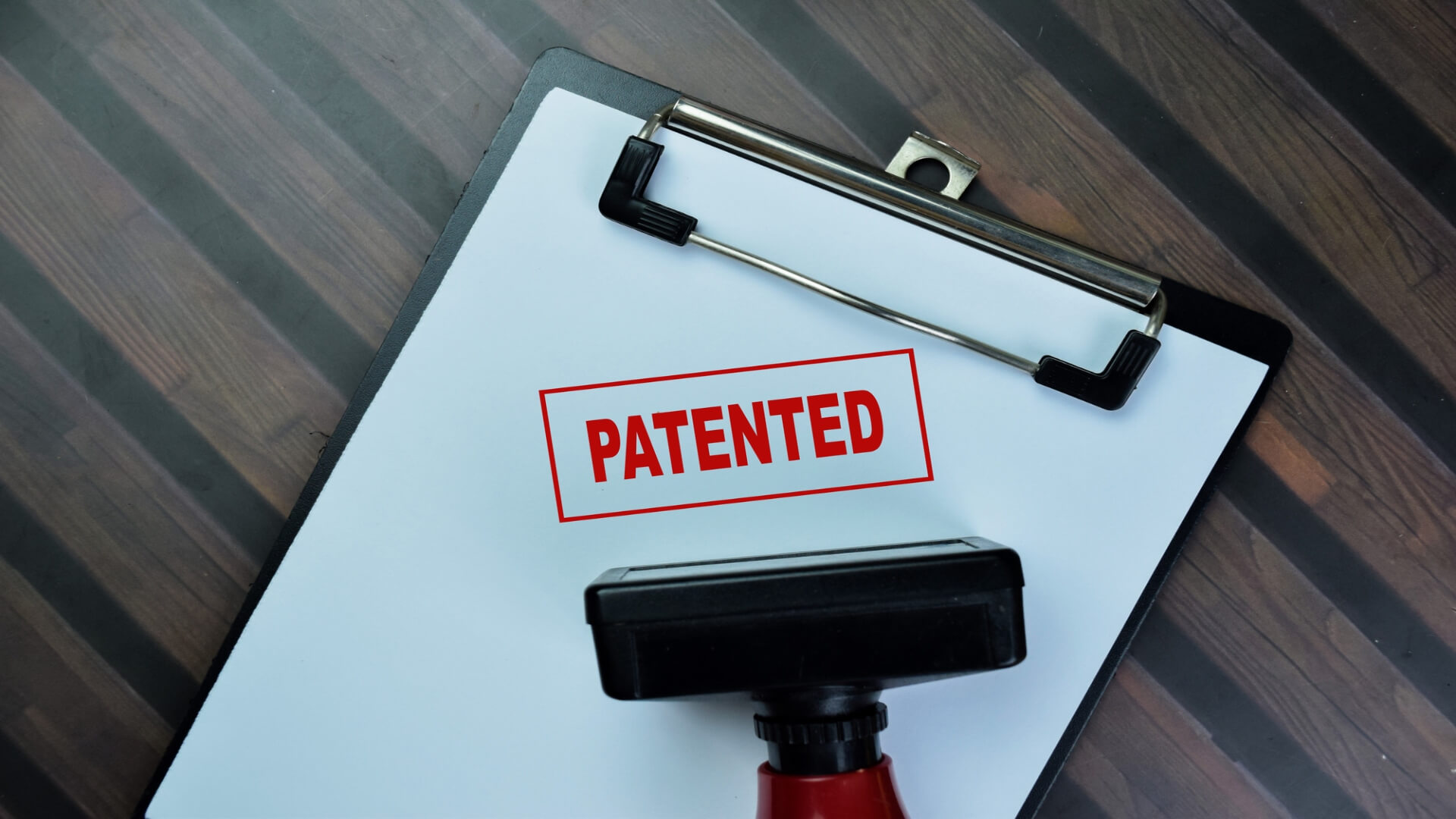White clipboard with the word patented stamped on it next to the rubber stamp