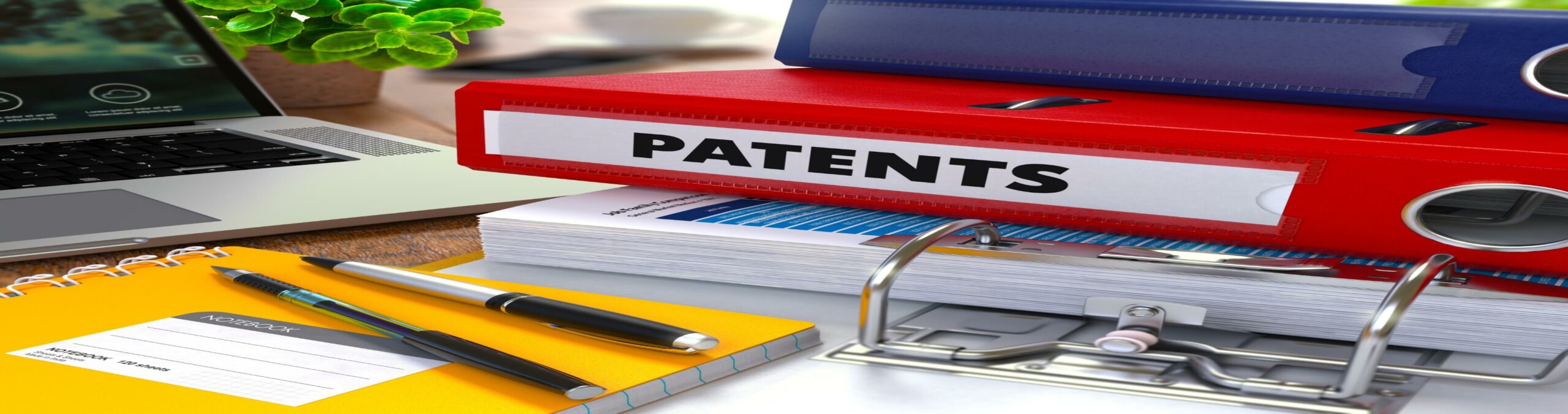 Red ring binder with a patent label next to a pad of paper with pens on top